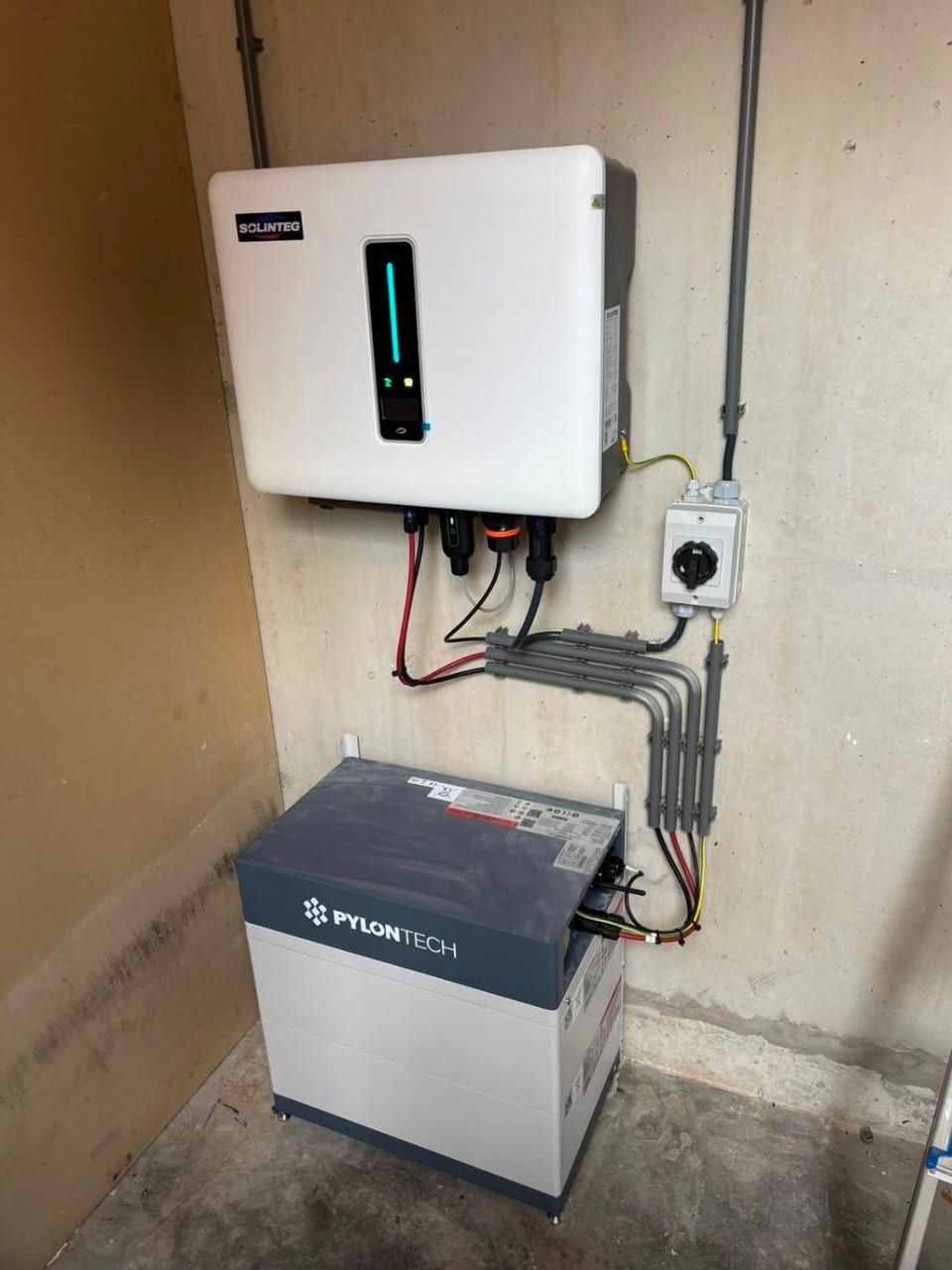 Solinteg omvormer boven een Pylontech batterijtoren met strak buiswerk tegen een betonnen garagemuur